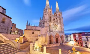 Majestuosa catedral de Burgos al anochecer, con sus agujas góticas iluminadas y el cielo azul crepuscular.