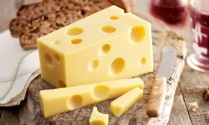 Ein Stück Emmentaler mit seinen charakteristischen Löchern, daneben Brot und ein Glas Rotwein. Die Herkunft des Käses ist unverkennbar.