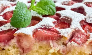 Puszyste ciasto jogurtowe z truskawkami, posypane cukrem pudrem i ozdobione listkiem mięty. Idealne na letni deser.
