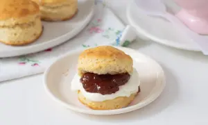 Un delicioso scone de reposteria inglesa, cubierto con crema y mermelada, listo para disfrutar.