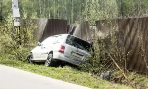 Srebrny minivan wjechał w drewniane ogrodzenie, powodując jego uszkodzenie. Pojazd jest częściowo wciśnięty w płot.