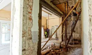 Remont wnętrza, pracownik na drabinie przy ścianie nośnej. Widać cegły i gruz.