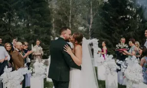Para młoda całująca się podczas ceremonii ślubnej na zewnątrz, otoczona gośćmi i dekoracjami.