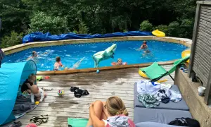 Barn njuter av en solig dag vid poolen, med en uppblåsbar haj och flytleksaker. En bebis leker i ett tält på altanen, perfekt för spf barn.