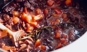 Herzhaftes Rindfleisch mit Tomaten und Rosmarin köchelt in einem Topf. Ein Holzkochlöffel rührt in der Soße. Perfekt für ein Bolognese Rezept.