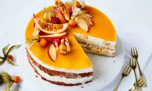 Eine leuchtend gelbe Pfirsich Maracuja Torte, dekoriert mit frischen Früchten und Physalis. Ein Stück ist herausgeschnitten, um die cremige Füllung zu zeigen.