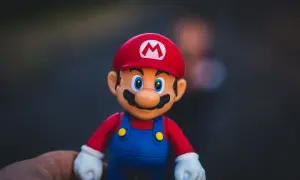 Figurka Mario w czerwonej czapce z literą M i niebieskich ogrodniczkach, trzymana na dłoni.
