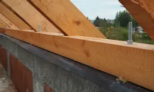Drewniana belka pod więźbą dachową, mocowana śrubami do betonowego muru.