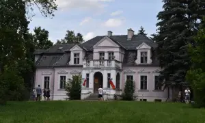 Różowy dworek Wybickich z polskimi flagami, otoczony zielenią.