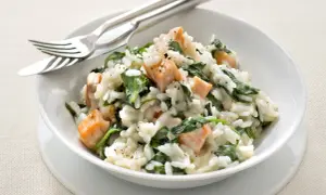 Un crémeux risotto épinard avec des morceaux de saumon. Un plat savoureux et coloré, prêt à être dégusté avec une fourchette et un couteau.