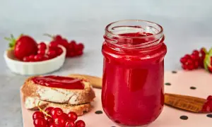 Glas mit Erdbeer Johannisbeer Marmelade, daneben Brot mit Marmelade und frische Beeren.