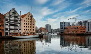 Widok na nabrzeże z zabytkowymi budynkami, żaglowcem i nowoczesną architekturą w tle.