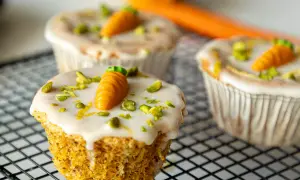 Drei leckere Karotten Muffins mit weißer Glasur, gehackten Pistazien und kleinen Marzipan-Karotten auf einem Gitter.