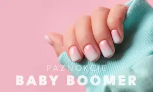 Dłoń z paznokciami w stylu baby boomer, delikatny gradient różu i bieli na jasnoróżowym tle.