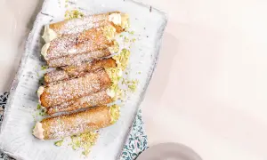 En bricka med flera italienska bakelser, cannolis, pudrade med florsocker och garnerade med hackade pistagenötter.