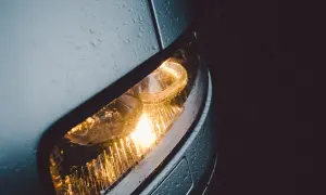 Światła postojowe samochodu świecą w deszczu. Krople wody na karoserii i kloszu lampy tworzą ciekawy efekt.