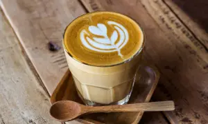 En vacker latte med mjölkskum som bildar ett mönster, serverad med en träsked. Perfekt kaffe för en mysig stund.