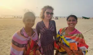 Trzy kobiety na plaży w Indiach. Jedna z nich trzyma pomarańczowy notes, może to notatnik do zapisywania cen rupii, czyli waluty w Indiach.