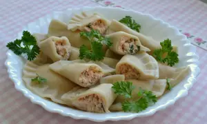 Pyszne pierogi z łososiem, delikatnie ugotowane, podane na białym talerzu z natką pietruszki.