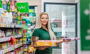 Kobieta w zielonej koszulce trzyma pudełka z pizzą na wynos w sklepie spożywczym.