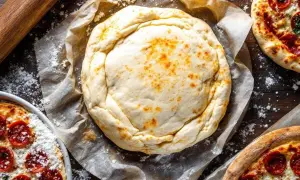Une pâte filo dorée, prête à être garnie, repose sur du papier cuisson. Autour, des pizzas au pepperoni et un rouleau à pâtisserie.