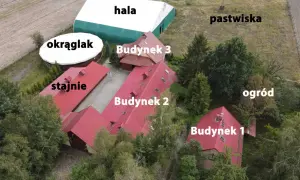 Widok z lotu ptaka na stadninę koni z budynkami, halą, okrąglakiem i pastwiskami.