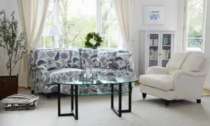 En ljus och inbjudande salong med en blommig Englesson fåtölj, soffa, soffbord och bokhylla.