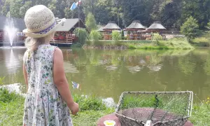 Dziewczynka w słomkowym kapeluszu patrzy na łowisko na wyspie Pokrzywna. Obok niej leży podbierak i kukurydza.