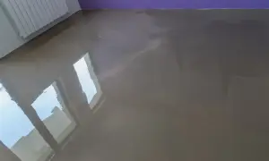 Lśniąca, szara posadzka anhydrytowa w nowym pomieszczeniu. Widać odbicia okien i kaloryfera.