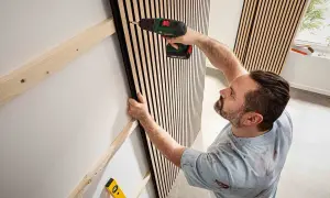 Man skruvar fast ribbpanel för att bygga akustikpanel på väggen.