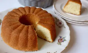 En gyllene, gammaldags sockerkaka med en bit borttagen, serverad på en vacker porslinsfat med blommor.