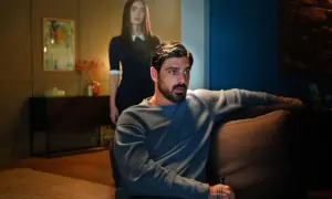 Michele Morrone w filmach, siedzi na kanapie, a za nim stoi kobieta.