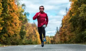 Un homme court sur une route bordée d'arbres aux couleurs d'automne, en plein effort, comme lors d'une séance fractionné.