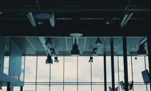 Ventilationsrör och lampor i taket, med en stor fönstervägg som visar en molnig himmel och en grönskande kulle. Kanske är det en plats där man kontrollerar radon nivåer.