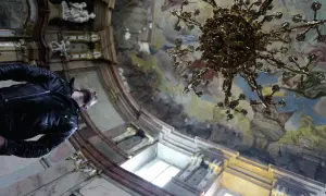 Mężczyzna w skórzanej kurtce podziwia freski i żyrandol w barokowym wnętrzu. Praga atrakcje zachwycają.