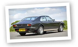 Klasyczny Aston Martin Lagonda w ciemnym kolorze, widziany z tyłu, na tle błękitnego nieba z chmurami.