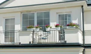 Białe okna pięknie komponują się z jasną, kremową elewacją budynku. Balkon ozdobiony kwiatami dodaje uroku.