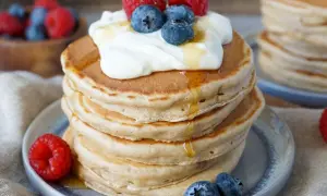 Stapel fluffiger Bananen Pancakes mit Honig, Joghurt, Himbeeren und Blaubeeren. Ein köstlicher Start in den Tag!