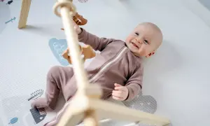 Uśmiechnięte dziecko leży na macie edukacyjnej pod drewnianym pałąkiem z zabawkami.