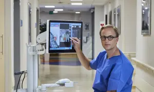Lekarz w niebieskiej koszuli wskazuje na ekranie komputerowym obraz z planowaniem biopsji gruczołu krokowego.