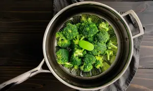 Frischer Brokkoli wird im Dampfgarer zubereitet. Ein grüner Griff liegt auf den Röschen.