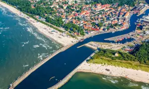 Widok z lotu ptaka na miasto i port, gdzie rzeka płynie przez Ustkę. Widać plażę, morze, falochrony i łodzie.