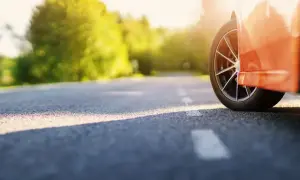 Pomarańczowy samochód na drodze, słońce przebija przez drzewa. Chcesz wiedzieć, jak szybko sprzedać samochód?