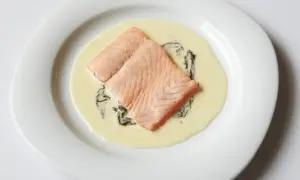 Deux pavés de saumon poêlés, nappés d'une onctueuse sauce oseille, servis sur une assiette blanche.