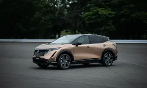 Elegancki, brązowy Nissan Ariya na tle zielonych drzew i asfaltu.