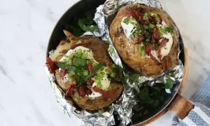Två härliga bakade potatisar med gräddfil, knaperstekt bacon och gräslök i en kopparpanna.