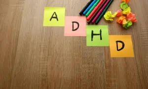 Kolorowe karteczki z literami A, D, H, D układają się w napis ADHD. Obok leżą flamastry i pogniecione kartki.