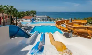 Vattenland på Kreta med färgglada rutschkanor som leder ner i en stor pool. Havet glittrar i bakgrunden.