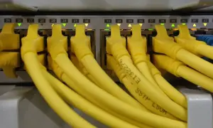 Conectores amarillos de red en un panel, cada uno con una luz verde o naranja encendida. Parece un splitter de red.