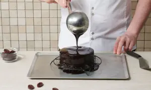 Un chef verse un glaçage miroir chocolat lait sur un gâteau rond. Le glaçage coule et brille, promettant une gourmandise exquise.